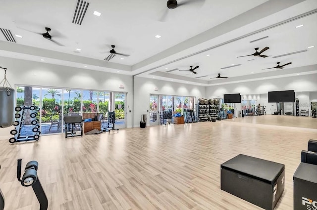 exercise room featuring a tray ceiling, a towering ceiling, and light hardwood / wood-style floors