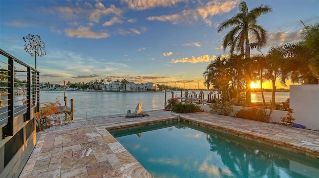 pool at dusk with a boat dock, a patio area, and a water view