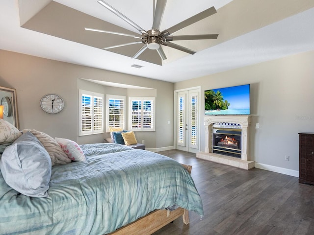 bedroom with ceiling fan, dark hardwood / wood-style floors, a raised ceiling, and access to outside