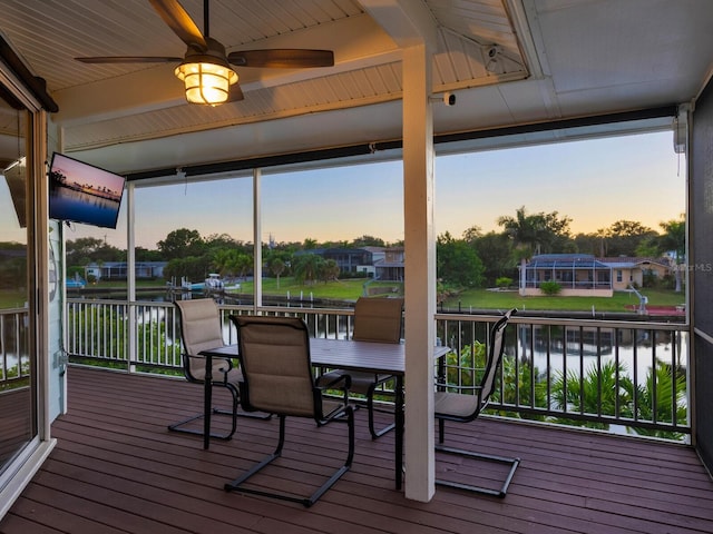 deck at dusk with a water view and ceiling fan