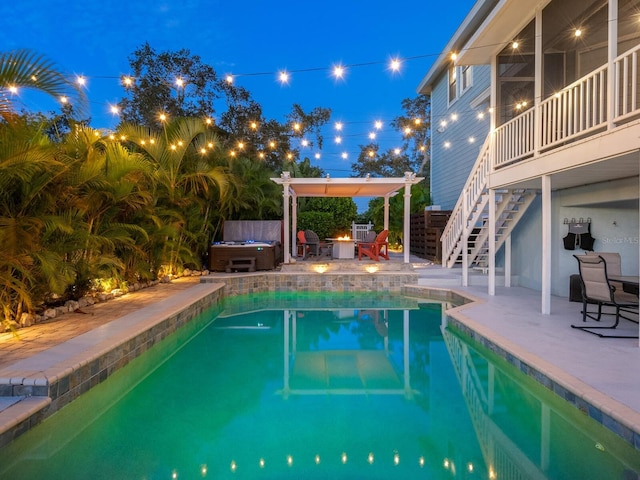 pool at twilight with a hot tub and a patio area