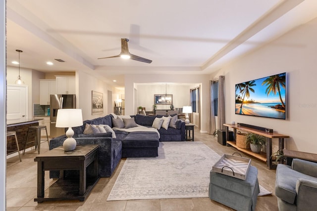 living room with ceiling fan with notable chandelier, a tray ceiling, and light tile patterned flooring