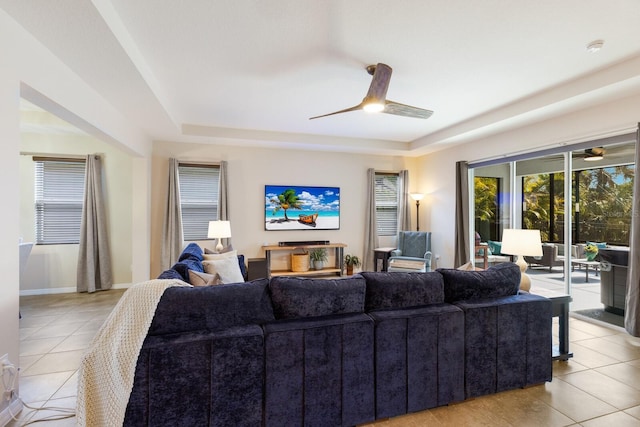 tiled living room with ceiling fan, plenty of natural light, and a tray ceiling