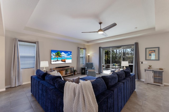 tiled living room with a raised ceiling and ceiling fan