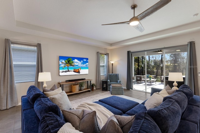 living room featuring a raised ceiling, light tile patterned floors, and ceiling fan