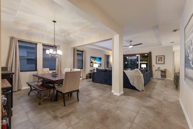 dining space with ceiling fan with notable chandelier and a tray ceiling