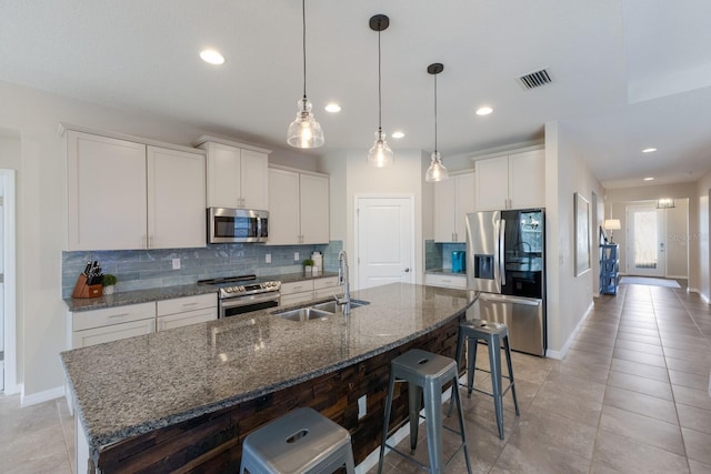 kitchen with sink, white cabinets, stainless steel appliances, and an island with sink