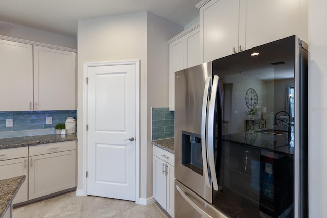 kitchen featuring stainless steel refrigerator with ice dispenser, backsplash, white cabinets, and dark stone countertops