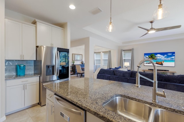 kitchen featuring appliances with stainless steel finishes, decorative light fixtures, white cabinetry, dark stone countertops, and sink