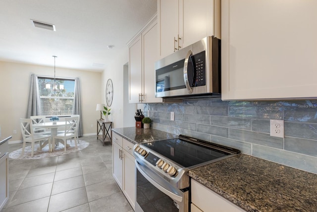 kitchen featuring stainless steel appliances, pendant lighting, white cabinetry, and dark stone counters