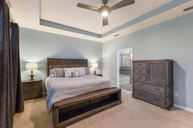 bedroom with ensuite bathroom, light colored carpet, ceiling fan, and a tray ceiling