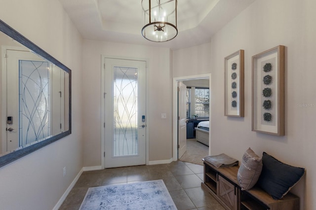 tiled foyer entrance with an inviting chandelier and a raised ceiling