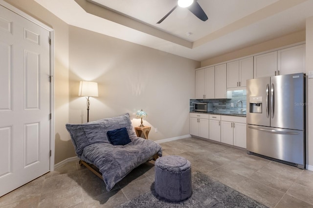 living area with ceiling fan, sink, and a tray ceiling