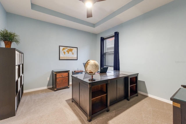 carpeted home office with a raised ceiling and ceiling fan