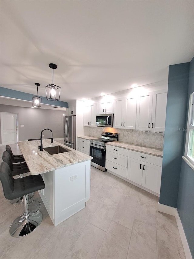 kitchen with sink, white cabinetry, stainless steel appliances, light stone counters, and decorative light fixtures