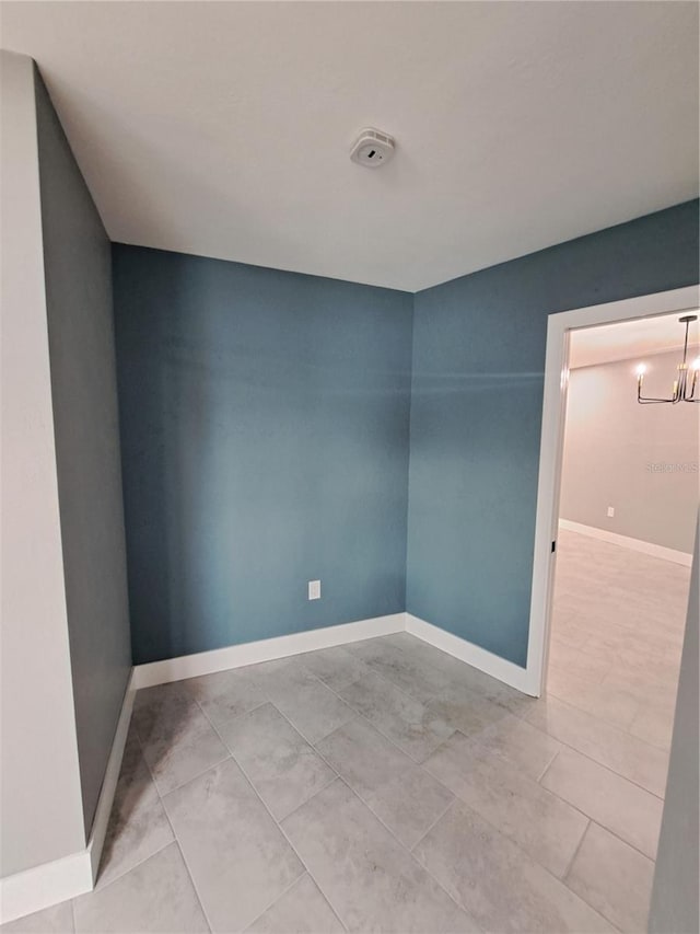 tiled spare room featuring a chandelier