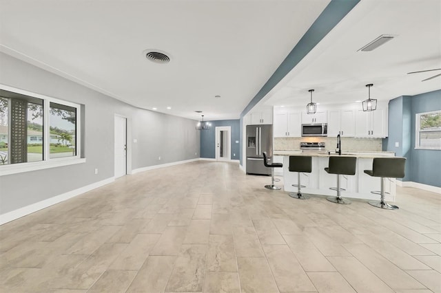 kitchen with pendant lighting, a kitchen island with sink, backsplash, stainless steel appliances, and white cabinets