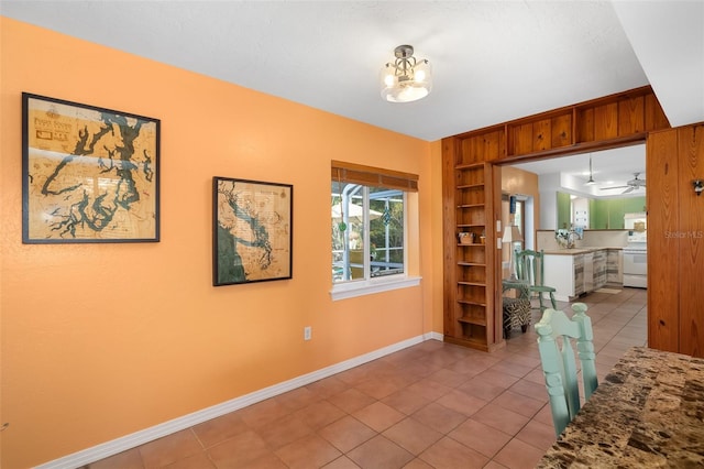 tiled dining room featuring built in features, ceiling fan with notable chandelier, and wooden walls