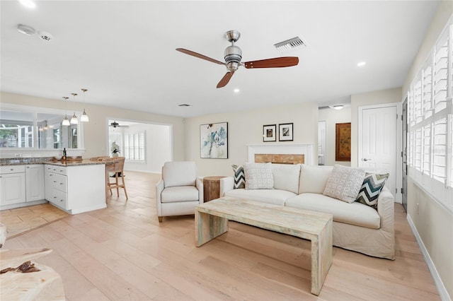 living room with a fireplace, ceiling fan, and light hardwood / wood-style flooring