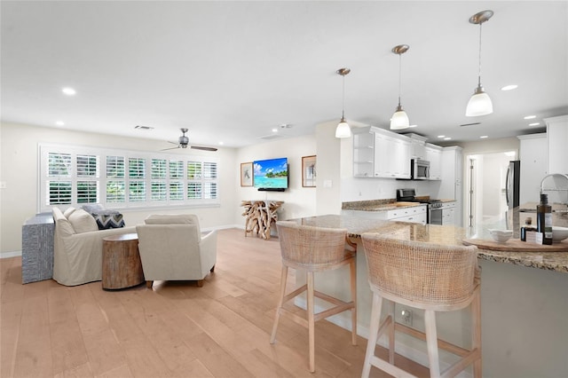 kitchen featuring white cabinets, a kitchen breakfast bar, hanging light fixtures, light wood-type flooring, and stainless steel appliances