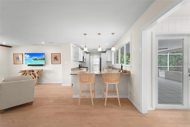 kitchen featuring light stone countertops, hanging light fixtures, kitchen peninsula, a kitchen bar, and white cabinets