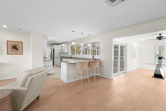 kitchen with pendant lighting, stainless steel fridge, light hardwood / wood-style floors, white cabinetry, and a breakfast bar area