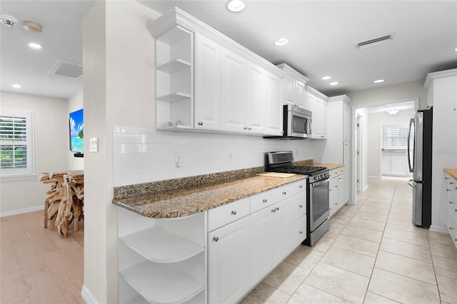 kitchen with a healthy amount of sunlight, stainless steel appliances, white cabinetry, and dark stone counters