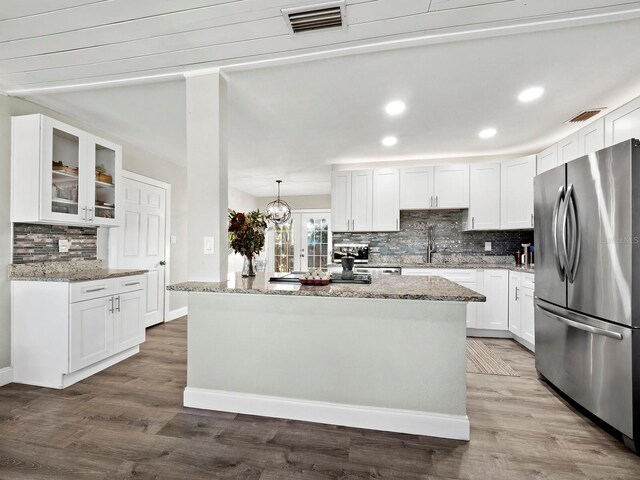 kitchen with pendant lighting, a center island, stainless steel fridge, light stone counters, and white cabinetry