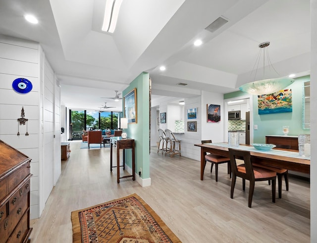 dining space with ceiling fan, a wall of windows, a tray ceiling, and light hardwood / wood-style flooring