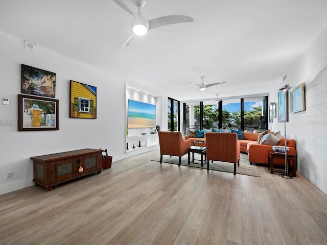 living room with ceiling fan, light hardwood / wood-style flooring, and a wall of windows