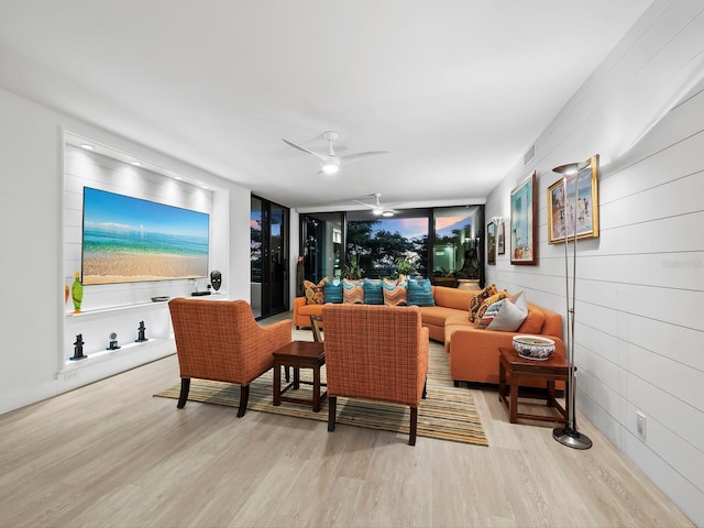 living room with ceiling fan, light hardwood / wood-style floors, and a wall of windows