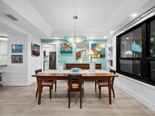 dining space with light wood-type flooring, a tray ceiling, and built in features