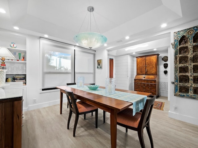 dining space with a raised ceiling and light wood-type flooring