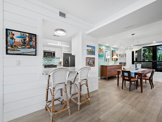 kitchen with stainless steel appliances, kitchen peninsula, decorative backsplash, white cabinets, and light wood-type flooring