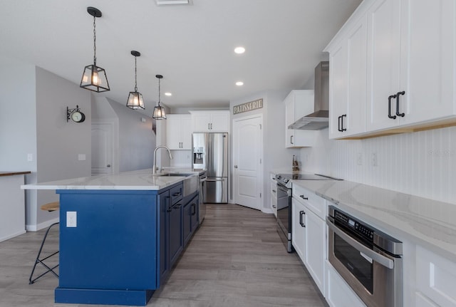 kitchen featuring wall chimney exhaust hood, stainless steel appliances, blue cabinets, a spacious island, and white cabinetry