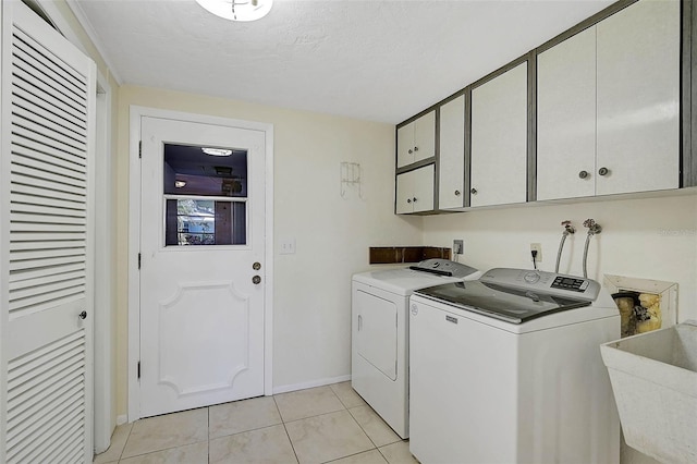 washroom with sink, cabinets, washing machine and dryer, a textured ceiling, and light tile patterned flooring