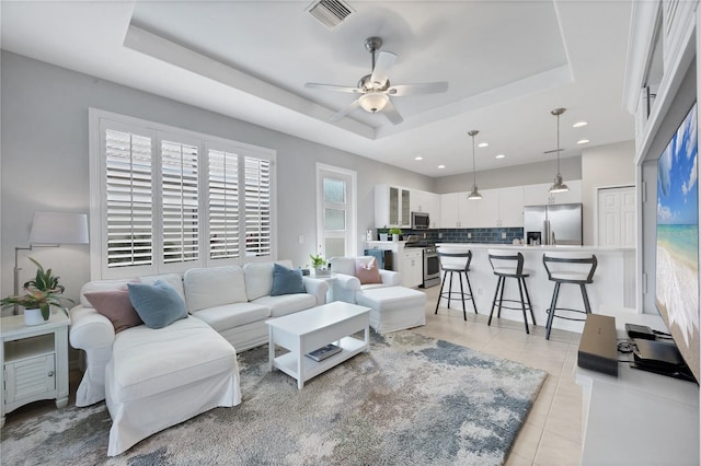 living room featuring ceiling fan, light tile patterned floors, and a tray ceiling