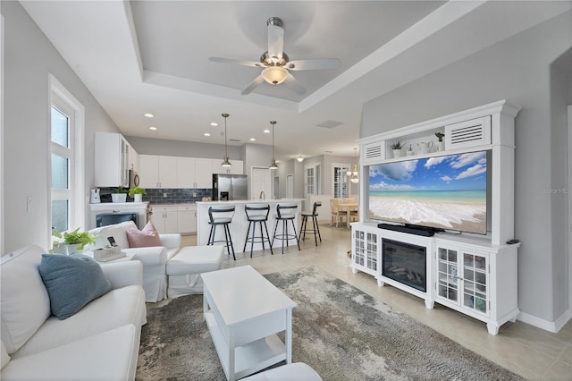 living room featuring a tray ceiling, ceiling fan, and light tile patterned flooring