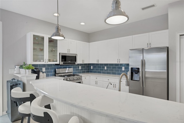 kitchen featuring a breakfast bar area, hanging light fixtures, white cabinets, and stainless steel appliances