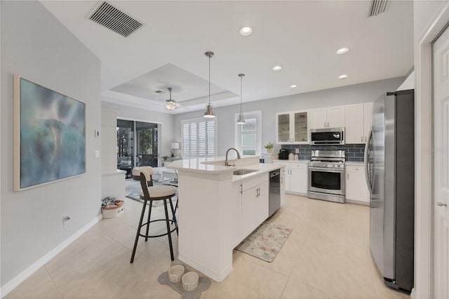 kitchen with stainless steel appliances, a raised ceiling, ceiling fan, a kitchen island with sink, and sink