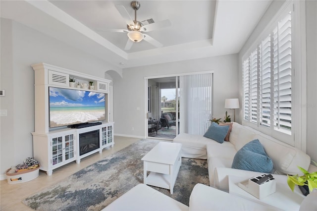 living room featuring a raised ceiling, light tile patterned floors, and ceiling fan