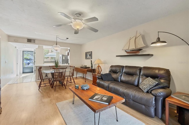 living room featuring ceiling fan with notable chandelier and light wood-type flooring