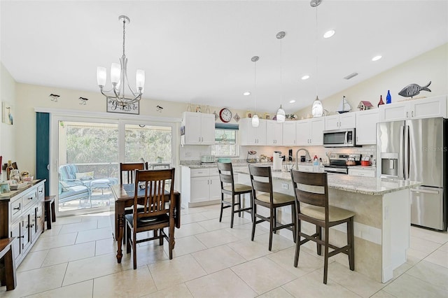 kitchen with decorative backsplash, appliances with stainless steel finishes, a kitchen island with sink, decorative light fixtures, and white cabinetry