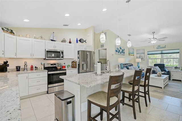 kitchen with a kitchen bar, appliances with stainless steel finishes, light stone counters, ceiling fan, and decorative light fixtures