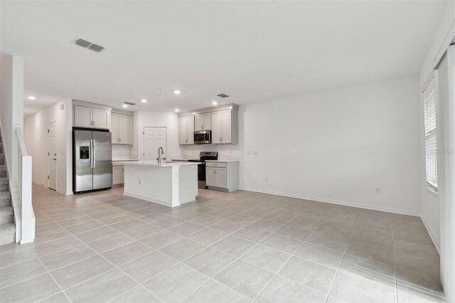 kitchen with light tile patterned flooring, sink, stainless steel appliances, and a center island with sink