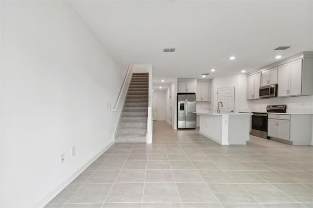 kitchen with light tile patterned floors, stainless steel appliances, sink, and a kitchen island with sink