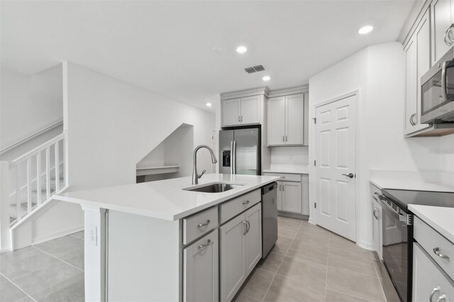 kitchen with gray cabinets, sink, a kitchen island with sink, stainless steel appliances, and light tile patterned floors