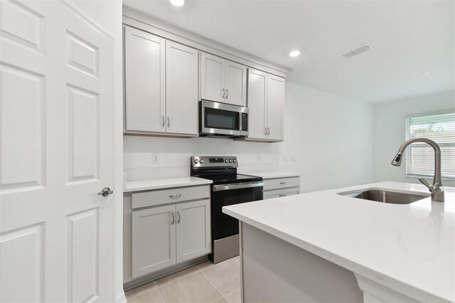 kitchen featuring sink, light tile patterned flooring, a kitchen island with sink, appliances with stainless steel finishes, and gray cabinetry