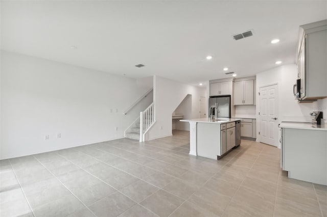 kitchen with a kitchen island with sink, appliances with stainless steel finishes, light tile patterned flooring, and gray cabinetry