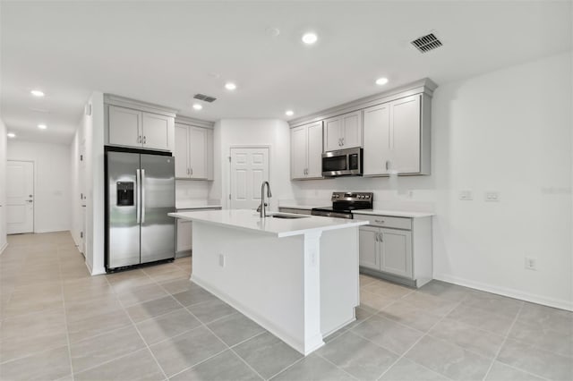 kitchen featuring gray cabinets, sink, a kitchen island with sink, appliances with stainless steel finishes, and light tile patterned floors